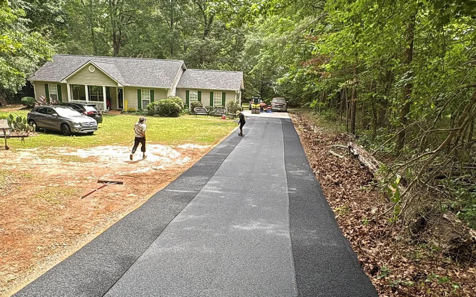 After: new asphalt driveway leading up to the house, crew finishing the edges