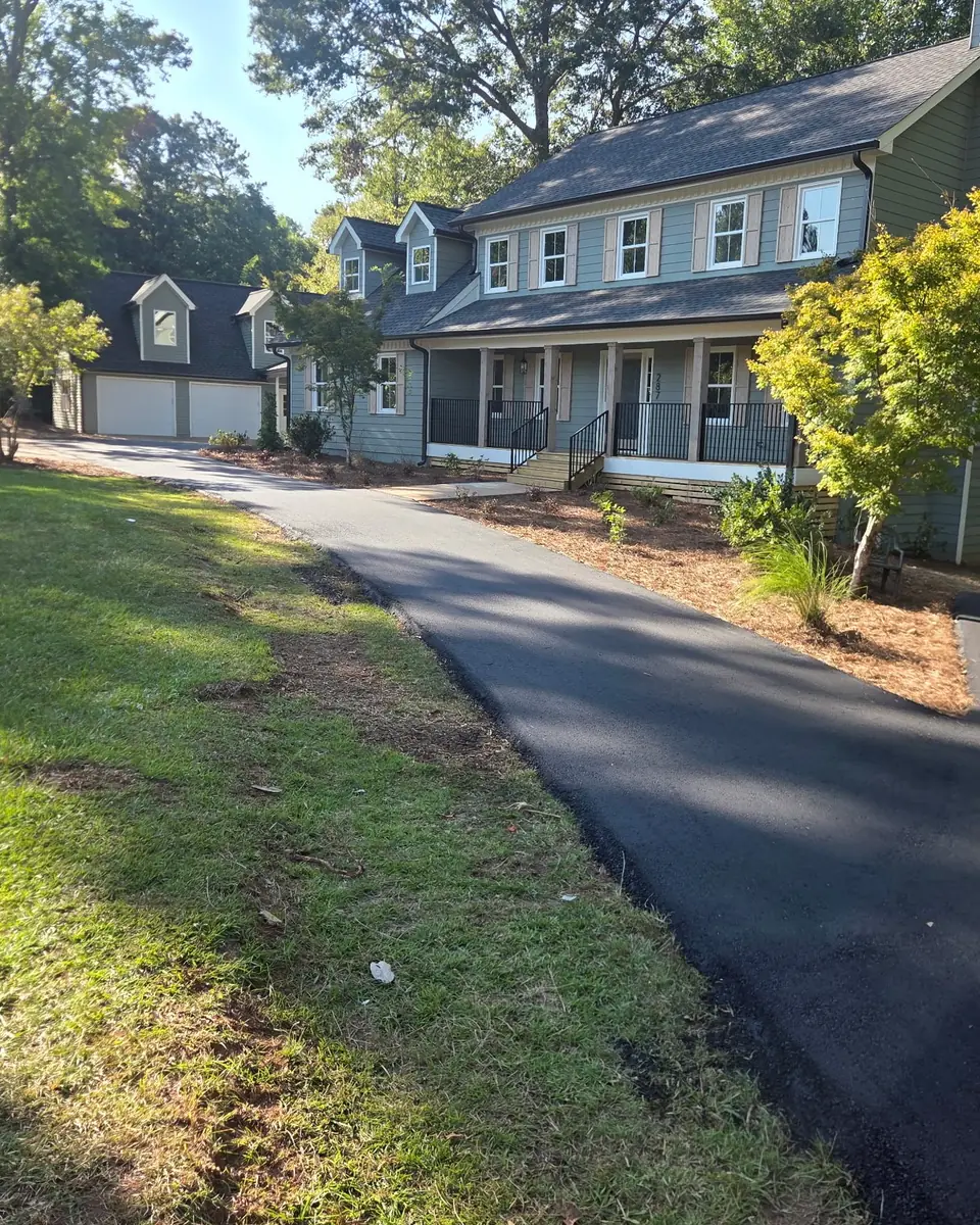 Long, freshly resurfaced asphalt driveway winding up to a two-story house after a mill and fill