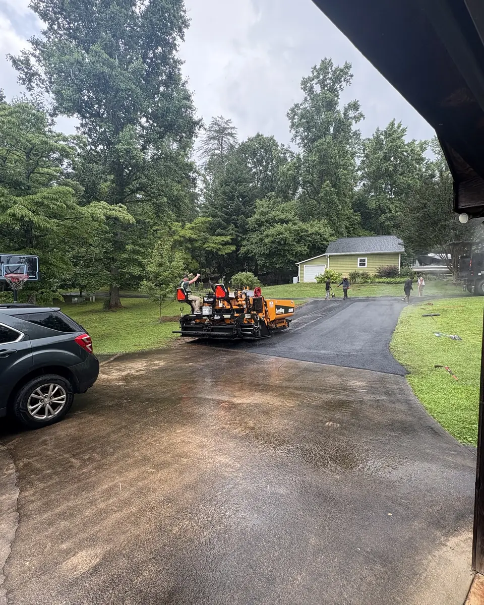 Paver and crew laying fresh asphalt up a residential driveway